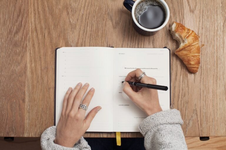 Writing morning plans in a notebook with coffee and croissant