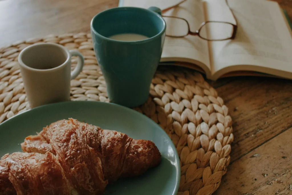 Coffee, croissant, and open book symbolizing small rewards and gamification focus for overcoming procrastination.