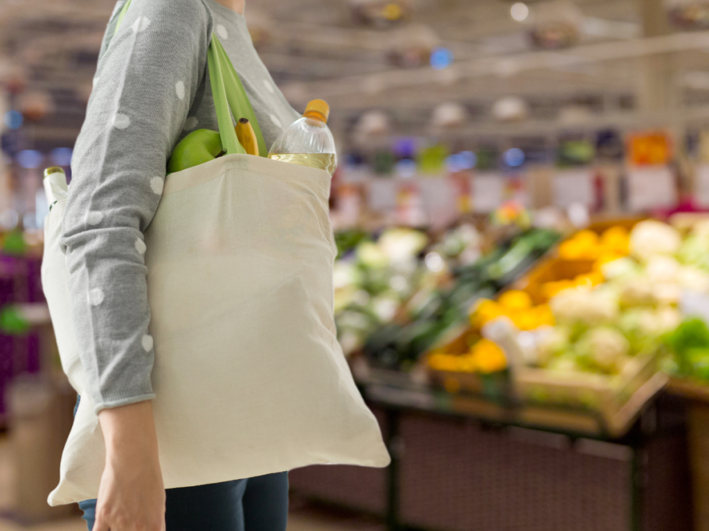 Person carrying a single tote bag while shopping in a grocery store, choosing simple items instead of using a cart.